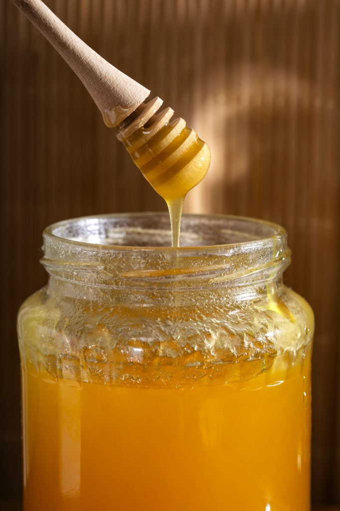 Glass jar of honey with wooden drizzler